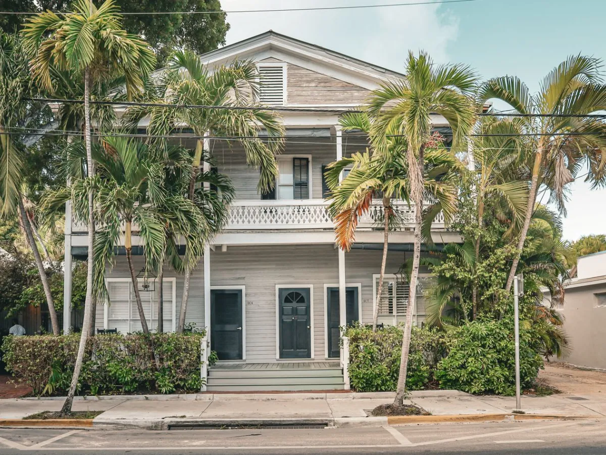 Two-story white house with palm trees and tropical shrubs out front